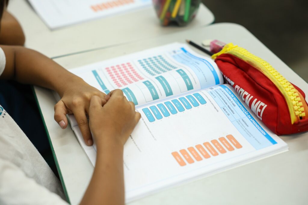 qualidade do ensino: mãos de um estudante sobre caderno de matemática em sala de aula.