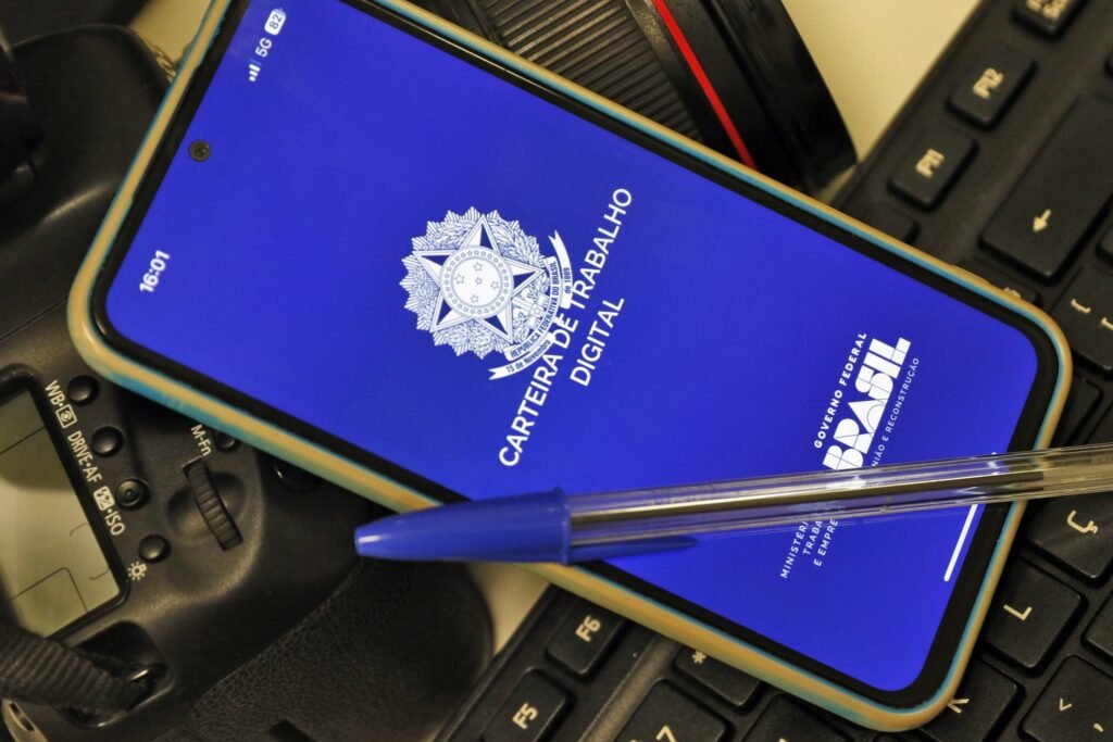 assedio eleitoral: smartphone exibindo a tela do aplicativo Carteira de Trabalho Digital ao lado de teclado e caneta.