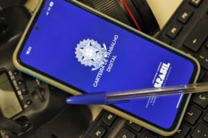 assedio eleitoral: smartphone exibindo a tela do aplicativo Carteira de Trabalho Digital ao lado de teclado e caneta.