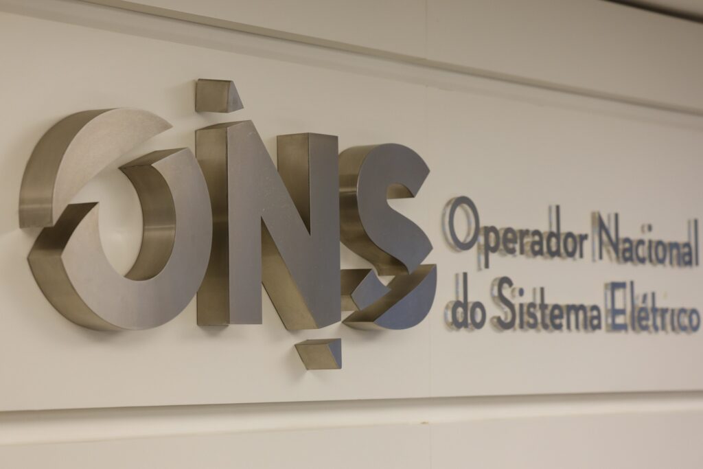 segundo turno: Logotipo metálico do Operador Nacional do Sistema Elétrico (ONS) fixado em parede branca.