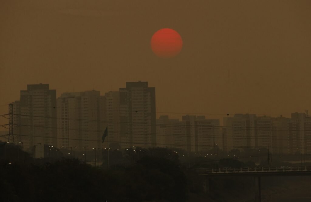 meta climatica: Prédios de São Paulo sob céu amarronzado por poluição com sol vermelho ao fundo.