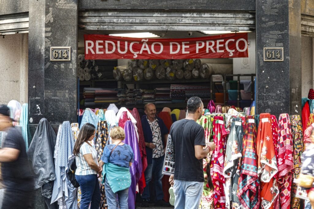 Monitor do PIB: Pessoas observam tecidos em uma loja de rua sob uma faixa de redução de preço.
