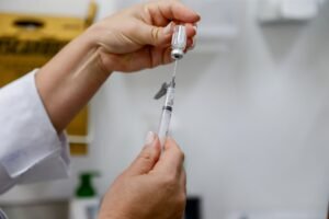 Profissional de saúde preparando vacinação contra a dengue com seringa e frasco.