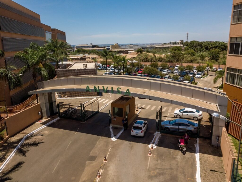 retatrutida: Vista aérea da entrada do prédio da Anvisa com arco metálico e letreiro verde.