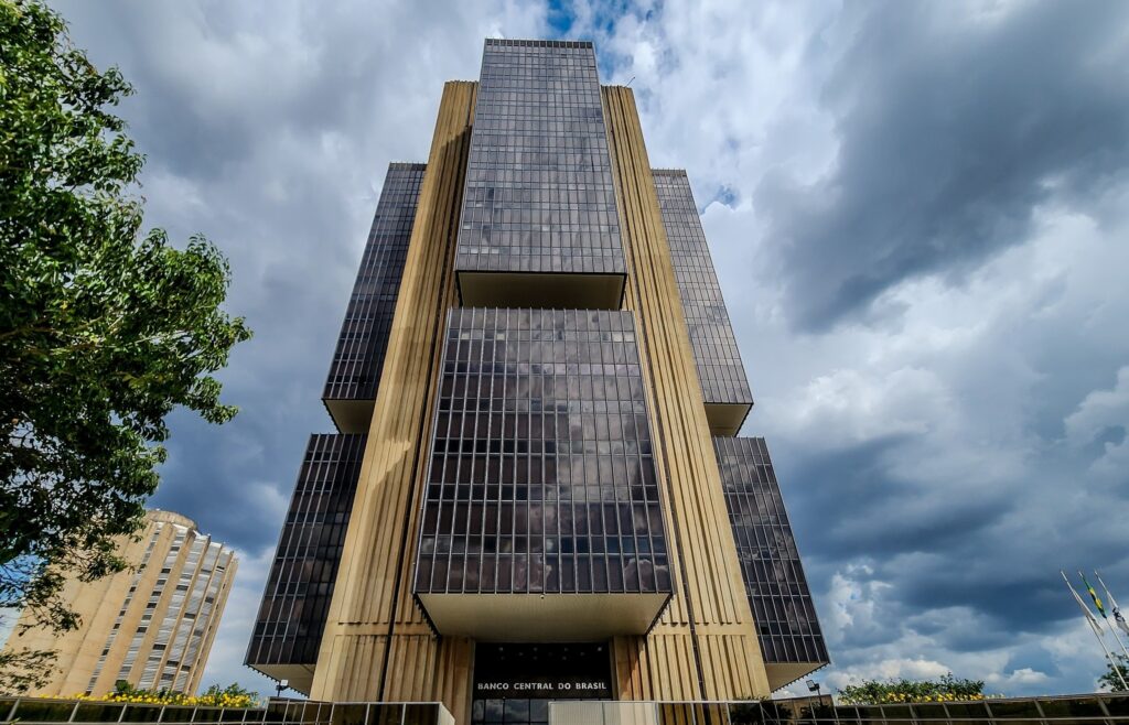 contas do banco central: Prédio do Banco Central do Brasil, visto de baixo para cima, com fachada de vidro e concreto sob um céu nublado.
