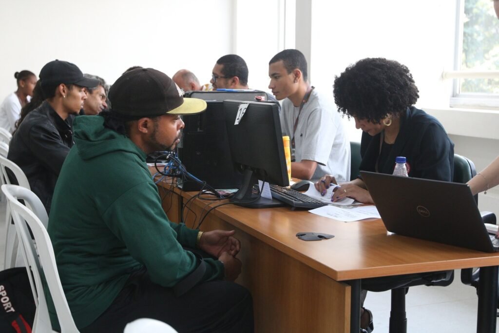 taxa de desocupacao: Pessoas em atendimento em mesas com computadores e laptops durante mutirão de emprego.