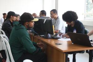 taxa de desocupacao: Pessoas em atendimento em mesas com computadores e laptops durante mutirão de emprego.
