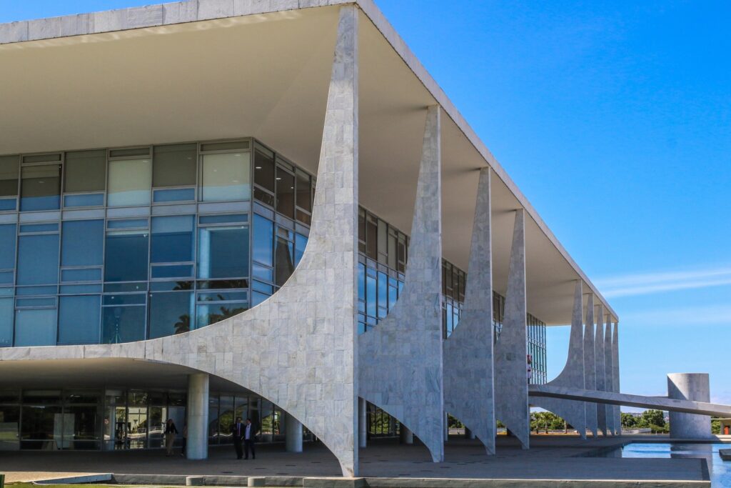 Fachada do Palácio do Planalto em Brasília, com colunas curvas de mármore branco e grandes painéis de vidro.