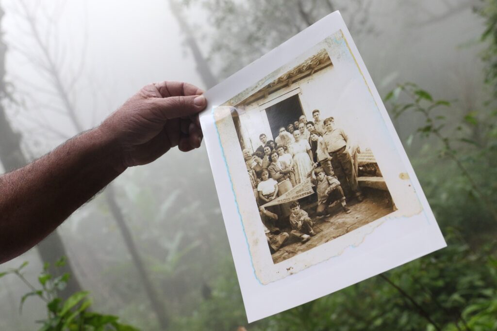 reparação quilombola: mão segura fotografia antiga em tom sépia de um grupo de pessoas em frente a uma casa.