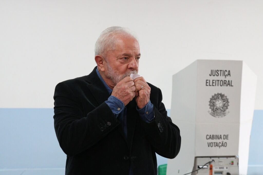 quebra de sigilo: Luiz Inácio Lula da Silva segura um pequeno papel próximo ao rosto ao lado de uma cabina de votação da Justiça Eleitoral.