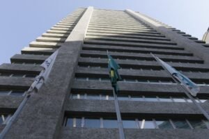 India Armelau: fachada do edifício da Alerj vista de baixo, com a bandeira do Brasil hasteada.