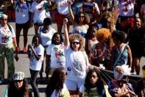 racismo contra Marielle Franco: Mulheres negras em marcha com punho erguido em protesto contra o preconceito.