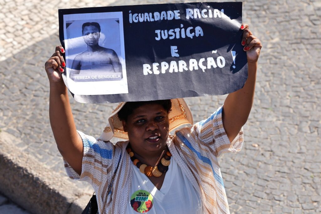 debate eleitoral: mulher negra segura cartaz com a foto de Tereza de Benguela e os dizeres de igualdade racial.
