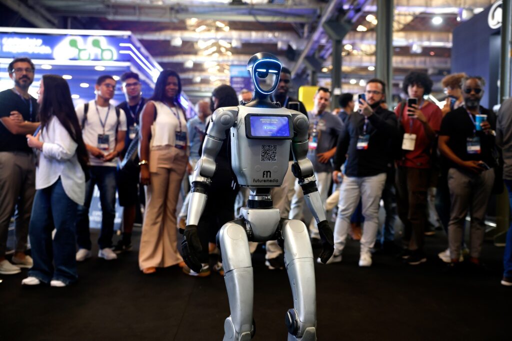 combater a desinformacao: robô prateado com tela interativa cercado por pessoas em pavilhão de inovação e tecnologia.