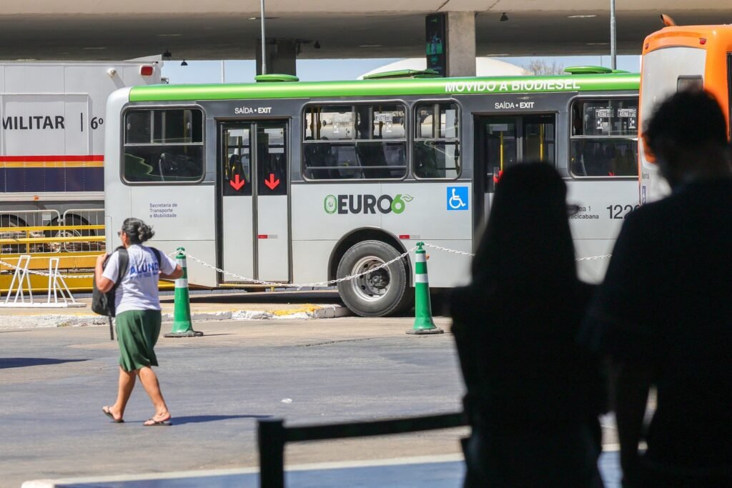 falta de onibus: Passageiros e ônibus em terminal rodoviário.