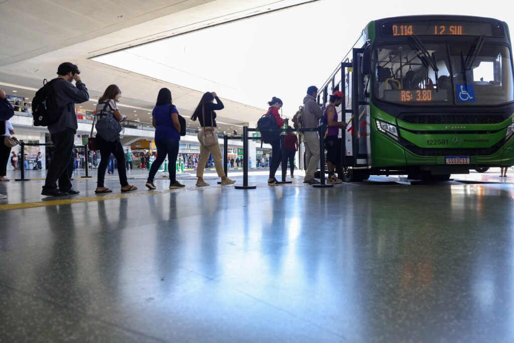 TRE-BA: Passageiros aguardam em fila para embarcar em um ônibus em terminal rodoviário.