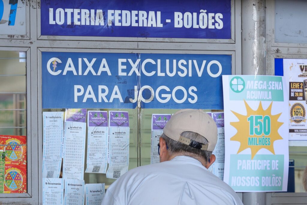 Homem de costas em frente a uma casa lotérica com placas "LOTERIA FEDERAL - BOLÕES" e "CAIXA EXCLUSIVO PARA JOGOS", e um cartaz anunciando "MEGA-SENA ACUMULA 150 MILHÕES".