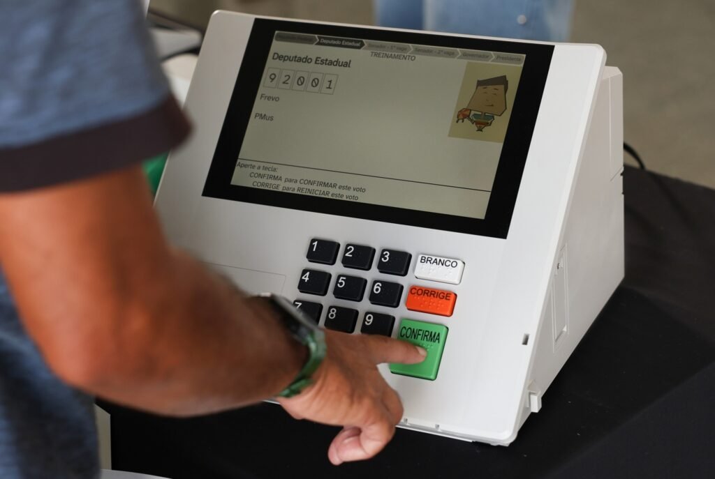 segundo turno: Mão de uma pessoa pressionando o botão "CONFIRMA" de uma urna eletrônica durante treinamento para eleição.