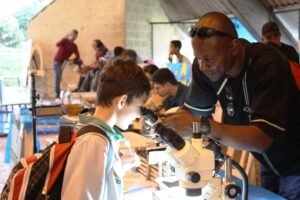 Programa Futuras Cientistas: estudante observa amostra em microscópio em feira de ciências.