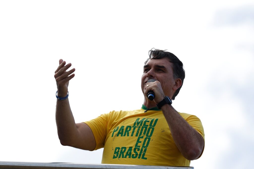 presidenciaveis: Flávio Bolsonaro fala ao microfone usando camiseta amarela com a frase "MEU PARTIDO É O BRASIL".