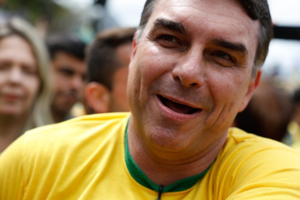 agenda dos presidenciaveis: Flávio Bolsonaro sorrindo, vestindo camiseta amarela, em plano fechado.