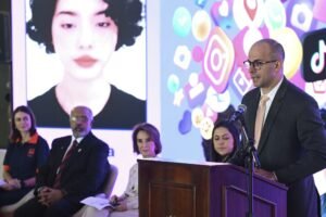bolsa familia: Homem discursa em púlpito com telão ao fundo exibindo ícones de redes sociais.