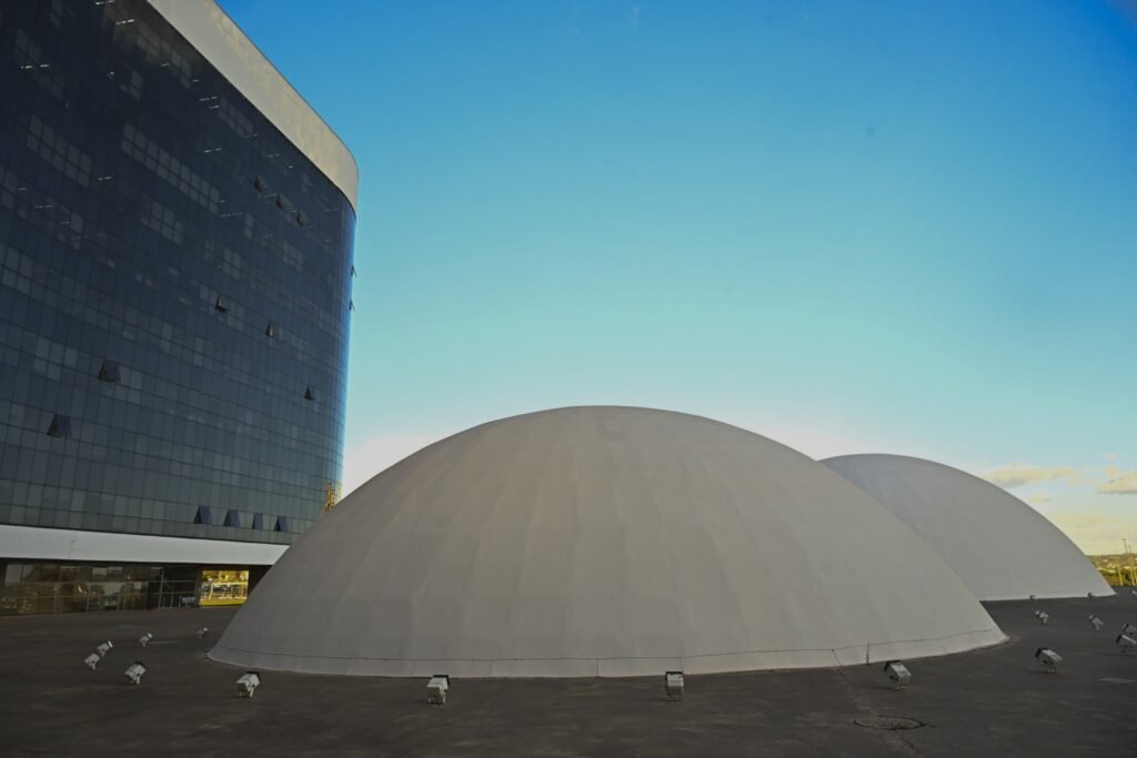 desfile de carnaval: fachada do Tribunal Superior Eleitoral com prédio espelhado e domos brancos sob céu azul.