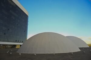 desfile de carnaval: fachada do Tribunal Superior Eleitoral com prédio espelhado e domos brancos sob céu azul.