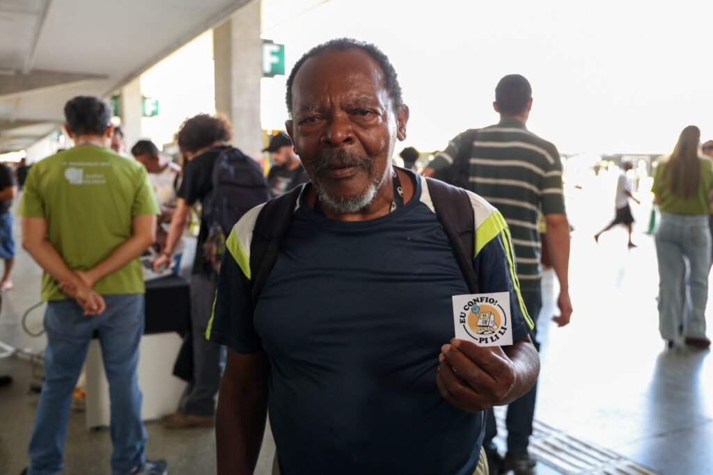 canais de WhatsApp: Homem segura cartão com a frase "EU CONFIO!" e ilustração de urna eletrônica em ação do TSE.