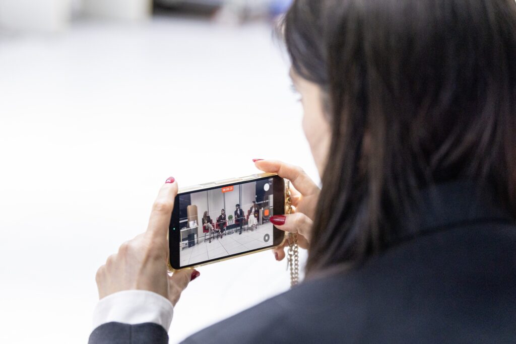 desinformação em saúde: pessoa grava com smartphone mesa redonda com participantes em evento institucional.