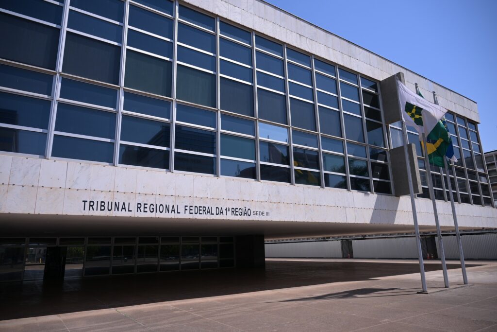 Fachada do edifício do Tribunal Regional Federal da 1ª Região (TRF-1) em Brasília, com grandes janelas de vidro e a inscrição identificando o local.