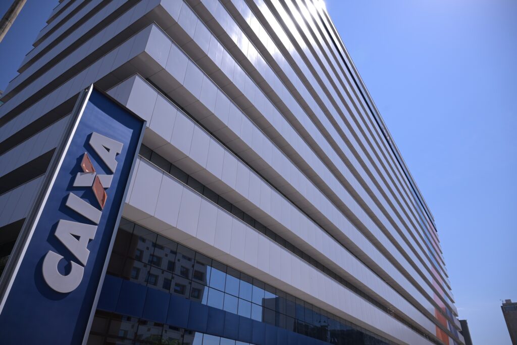 devolução de bets: Fachada de edifício moderno com totem azul exibindo a palavra "CAIXA" sob céu azul.