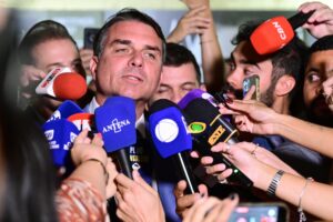Flávio Bolsonaro concede entrevista a jornalistas, cercado por diversos microfones de emissoras como "CBN", "BNC" e "ANTENA".