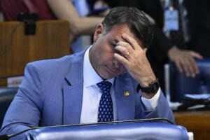 Senador Flávio Bolsonaro com a mão na testa e expressão pensativa durante sessão no Plenário do Senado.