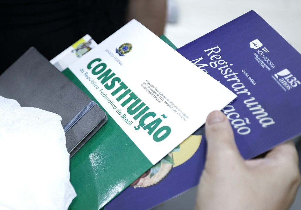 ata notarial: Mãos seguram exemplares da Constituição Federal do Brasil e cartilhas institucionais.