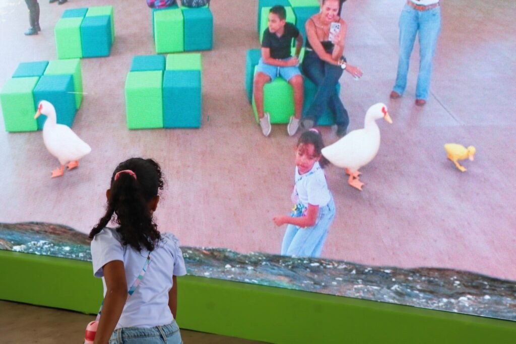 brinquedos com IA: criança de costas observa tela que exibe patos e pessoas em blocos de espuma coloridos.