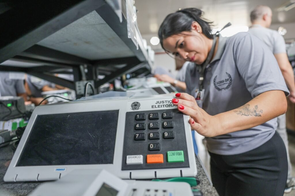 locais de votação: servidora do TRE-DF realiza procedimento em urna eletrônica com a inscrição "JUSTIÇA ELEITORAL".