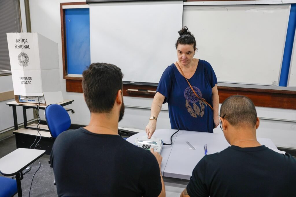 eleicoes: mulher vota em urna eletrônica acompanhada por dois homens em seção eleitoral na UERJ, no Rio de Janeiro.