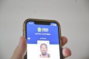 Aplicativo e-Título aberto em smartphone exibindo o brasão nacional, a identificação da Justiça Eleitoral e um documento de identidade digital com foto.