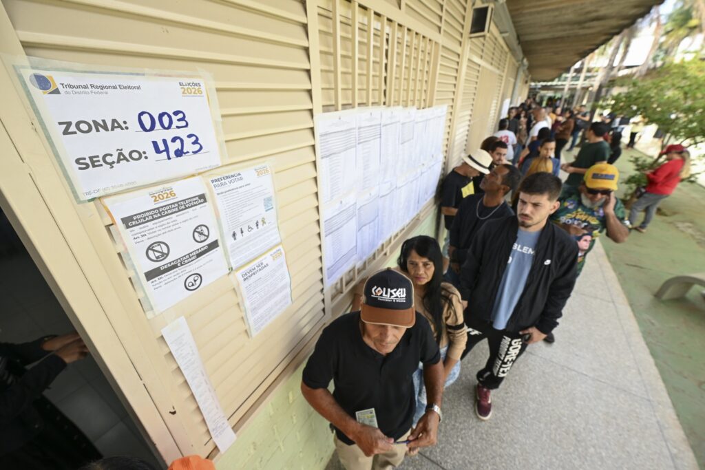 horário de votação: eleitores aguardam em fila ao lado de avisos informativos em zona eleitoral.
