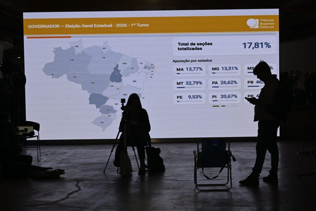 apuração do 2° turno: silhuetas de pessoas diante de painel eletrônico com dados no Tribunal Superior Eleitoral.