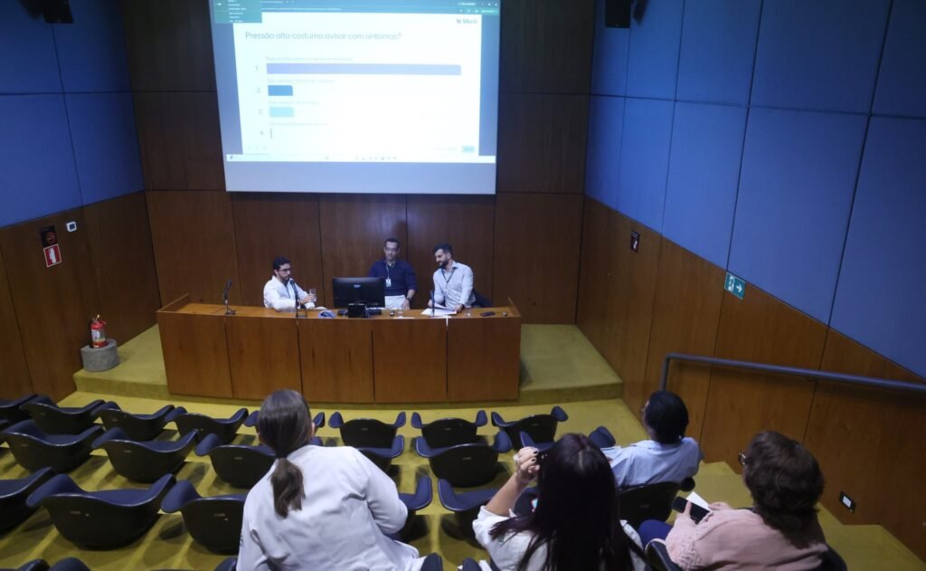 hipertensão em crianças: Três homens em um auditório realizam uma apresentação sobre pressão alta e prevenção.