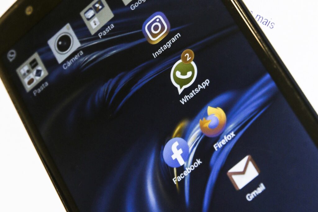 Seletividade algorítmica: Tela de smartphone exibindo ícones de aplicativos como "WhatsApp", "Instagram", "Facebook", "Firefox" e "Gmail" sobre fundo azul abstrato.