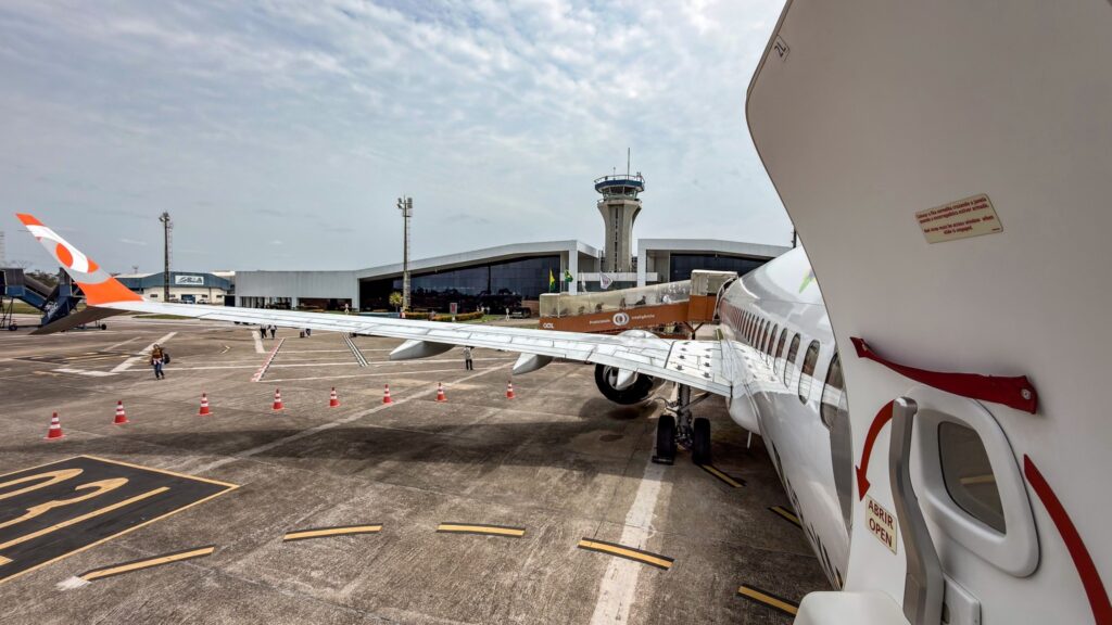 combustível sustentável: avião comercial estacionado no pátio de aeroporto com terminal ao fundo.