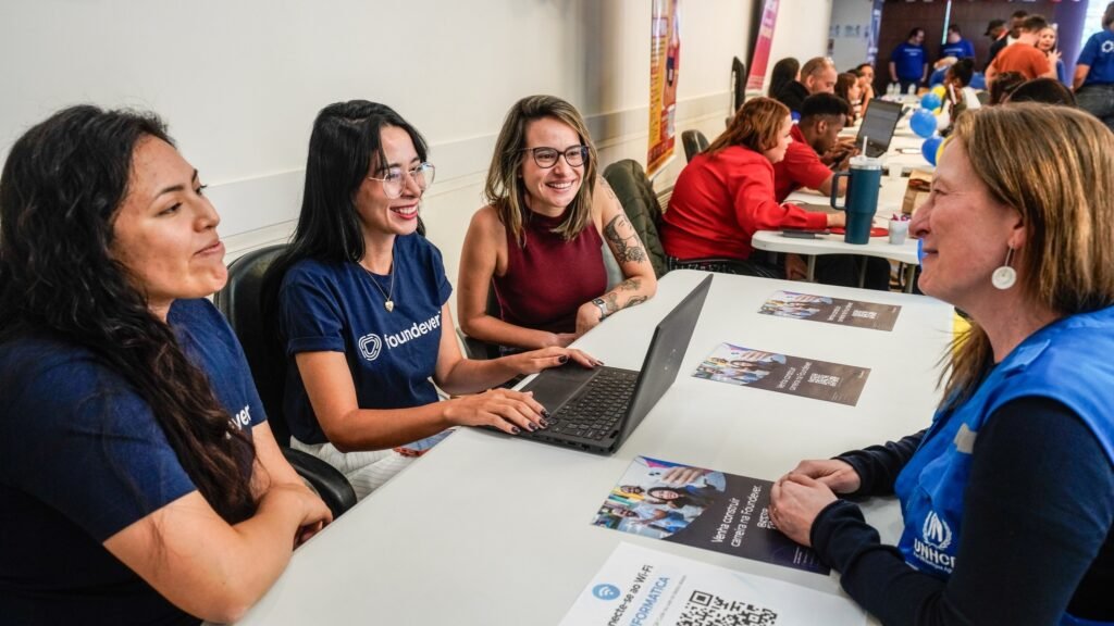 Mulheres conversam e utilizam notebooks em ação de empregabilidade para refugiados em São Paulo.