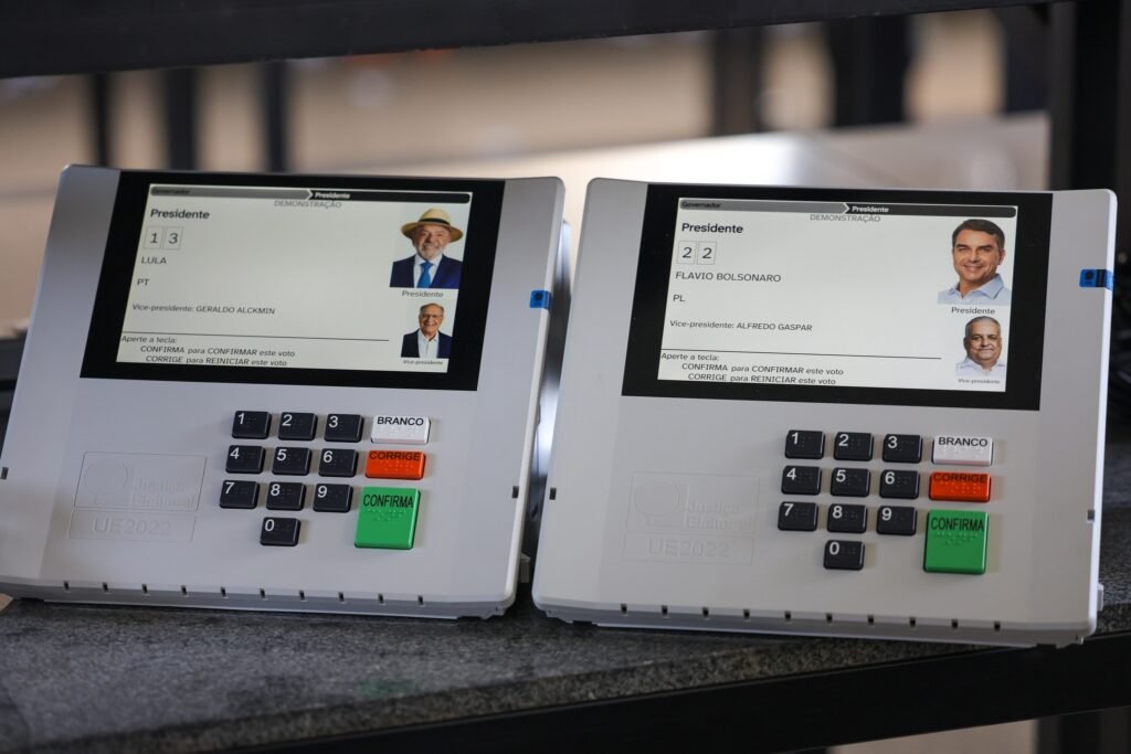 quebra de sigilo bancário: Duas urnas eletrônicas lado a lado em modo de demonstração com candidatos à presidência.