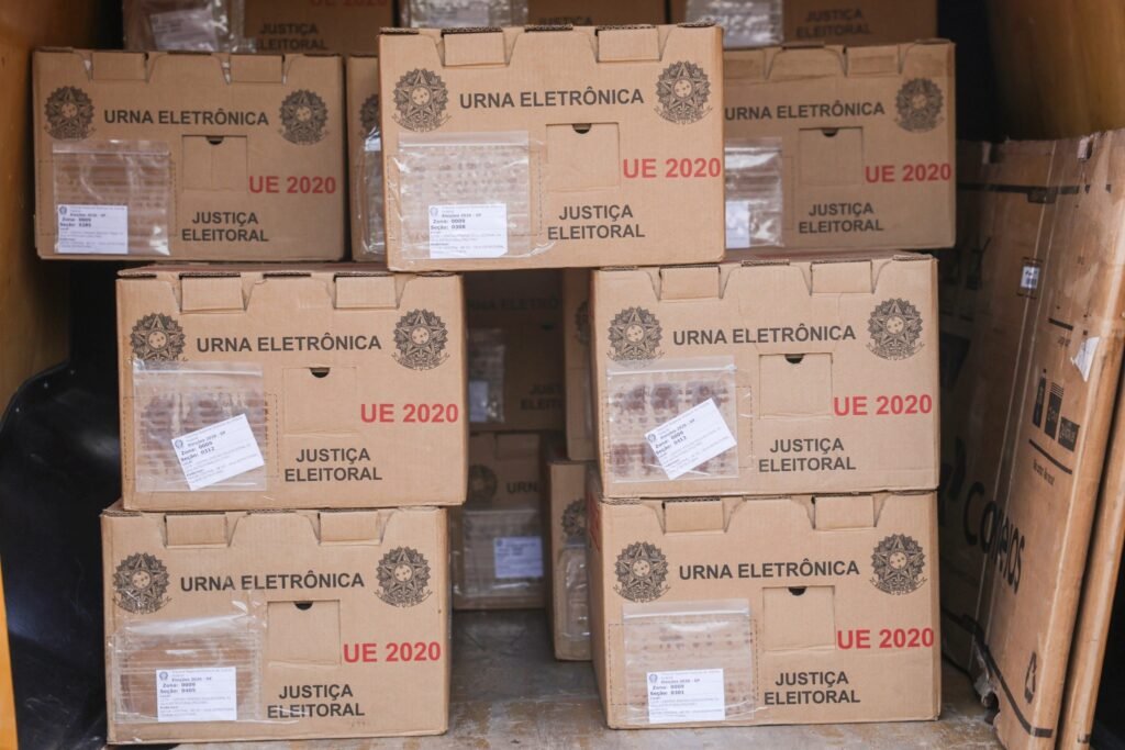 forcas armadas: Caixas de papelão contendo urnas eletrônicas e materiais para votação organizadas no interior de um veículo de transporte.