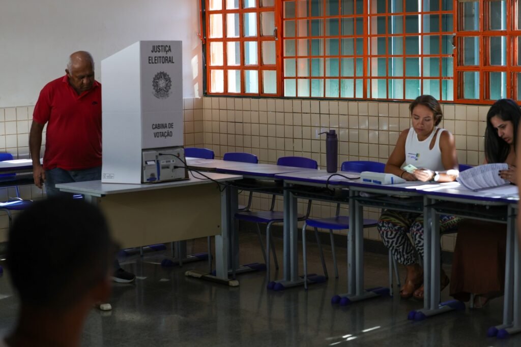 Eleitores em seção eleitoral com cabine de votação da Justiça Eleitoral.
