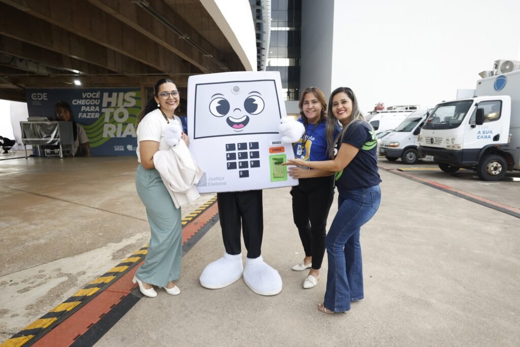 Lorenzo Pazolini: Três pessoas posam com mascote da Justiça Eleitoral durante cobertura das eleições 2026