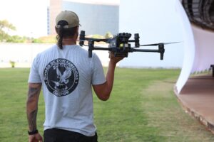 interferência externa: Agente com camiseta da Polícia Federal carrega drone em área verde.